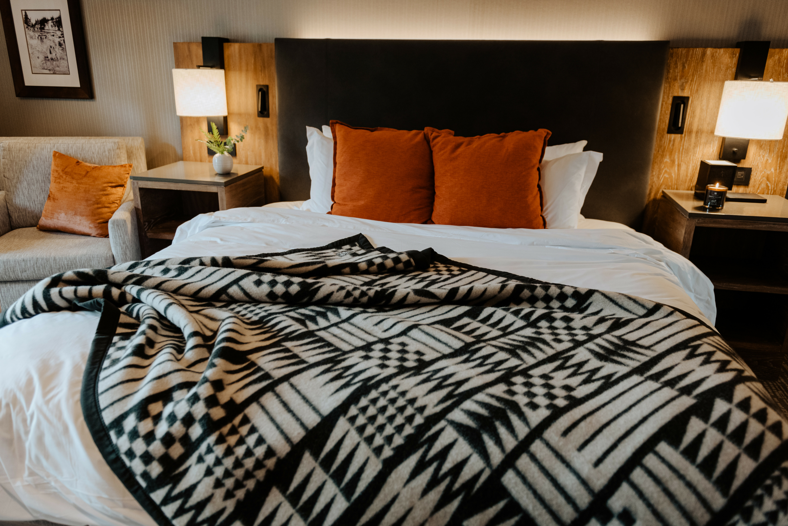 Coast Salish black and white patterned wool blanket laid across a bed with white blanket underneath and red pillows