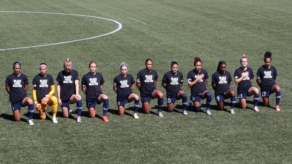 NWSL soccer players taking a knee during the national anthem.