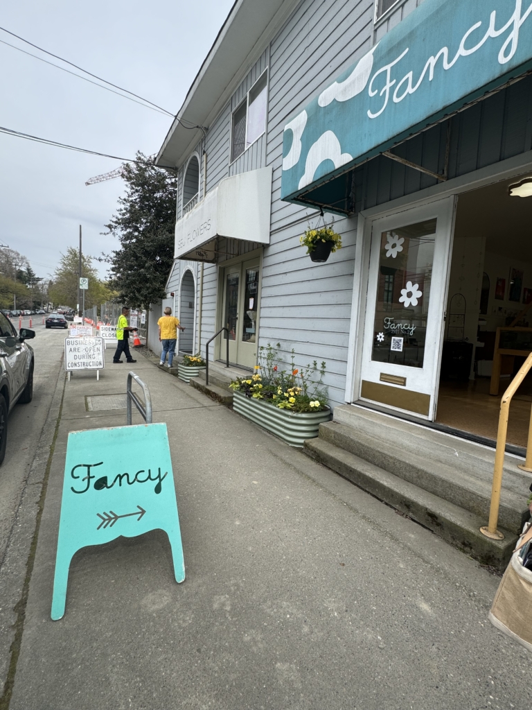 This photo depicts a bright blue sandwich board sign in front of Fancy's storefront.